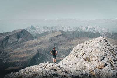 Man standing on rock looking at mountains against sky