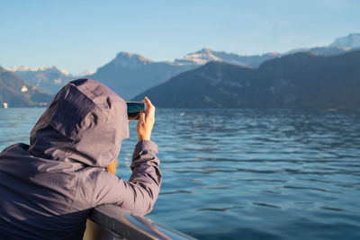 Close-up of woman photographing sea through mobile phone against mountain