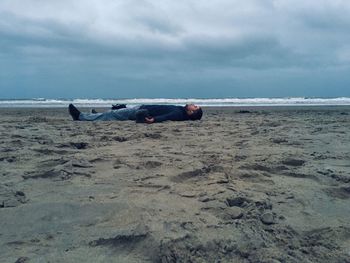 Man lying on beach against sky