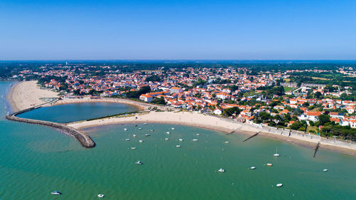 High angle view of cityscape by sea against clear blue sky