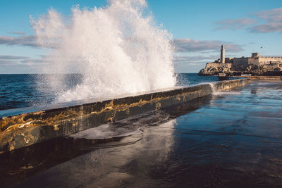 Waves splashing on shore against sky