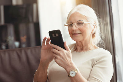 Senior woman using smart phone while sitting at home