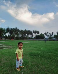 Rear view of boy standing on field against sky