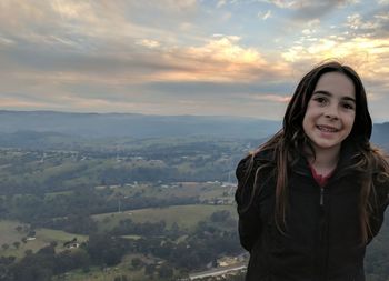 Portrait of girl smiling while standing against landscape during sunset