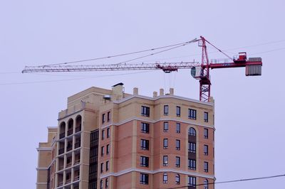 Low angle view of crane by building against sky