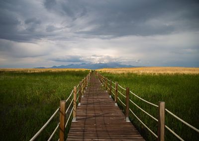 View of wooden boardwalk on field against sky