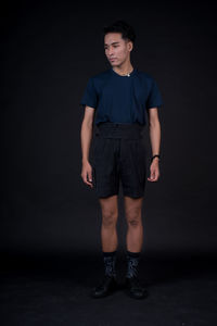 Portrait of young man standing against black background
