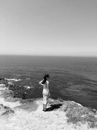 Rear view of woman standing at beach against clear sky