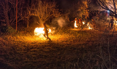 People standing by fire in forest at night