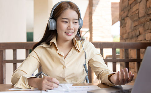 Portrait of smiling young woman using phone while sitting on table