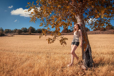 Young woman standing by tree on field against sky