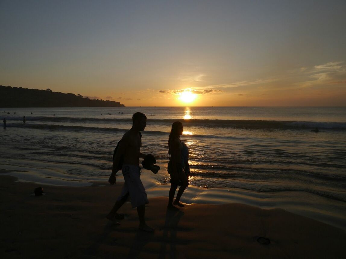 SILHOUETTE COUPLE WALKING ON BEACH AGAINST SUNSET SKY