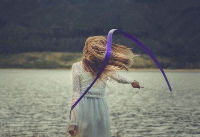 Rear view of woman twirling ribbon by lake