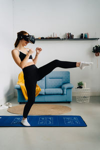 Side view full length of fit anonymous female in sportswear performing kicks on mat while training in vr headset at home