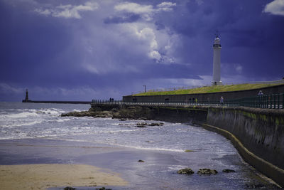 Lighthouse amidst sea and buildings against sky