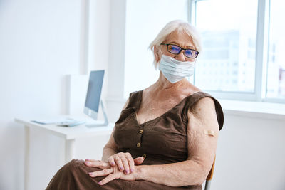 Portrait of senior woman wearing mask while sitting at hospital