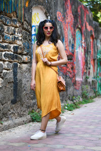 Full length of fashionable young woman standing on footpath against graffiti wall