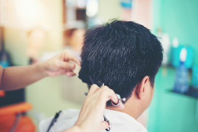 Rear view of woman cutting man hair in salon