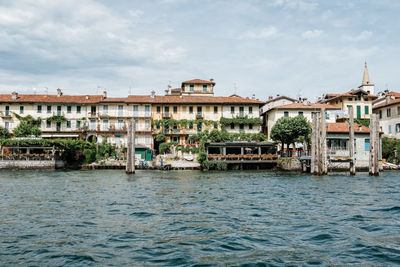 Buildings at waterfront against cloudy sky