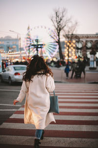 Rear view of young woman crossing road in city in winter