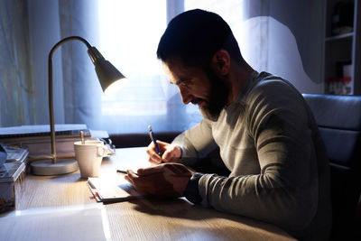 Young white man with a neat beard studying and looking at the phone at his desk