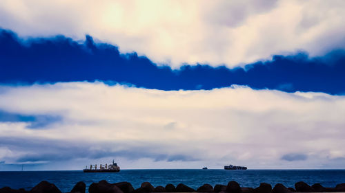 Silhouette of boats in sea against cloudy sky