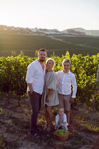 Family with children, boys, stands in a grape field at sunset with a basket of green berries