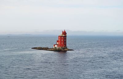 Lighthouse on sea by building against sky