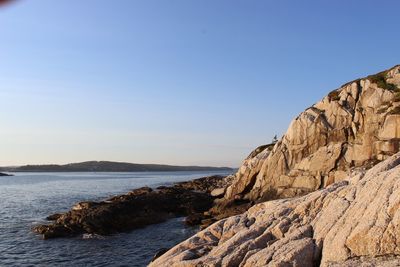 Rock formations by sea against clear blue sky