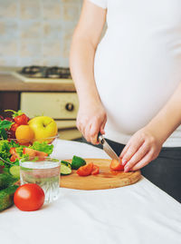 Midsection of pregnant woman cutting tomatoes