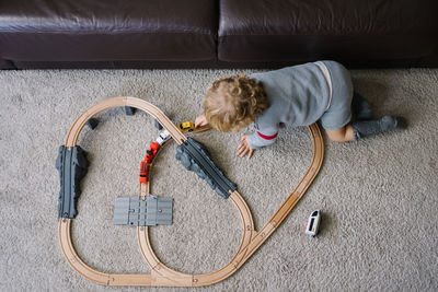 Top view of unrecognizable curly haired little kid playing with toy road and cars on carpet at home