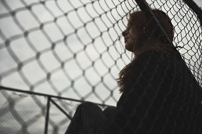 Rear view of woman looking through chainlink fence