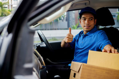 Young delivery man sitting in car with parcel box