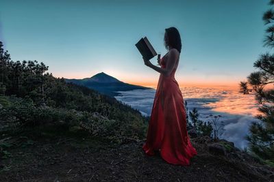Woman standing on rock against sky during sunset