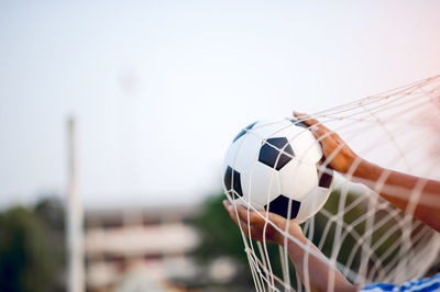 Cropped hands of man holding ball in soccer goal against clear sky