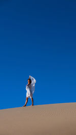 Young woman standing on sand at desert against clear blue sky