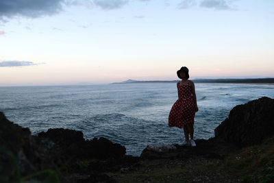 Rear view of woman standing on beach against sky during sunset