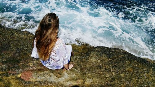 High angle view of woman sitting on rock by sea