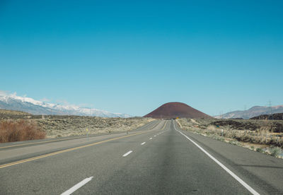 Empty road leading towards mountains against clear blue sky