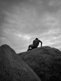 Low angle view of man sitting on rock against sky