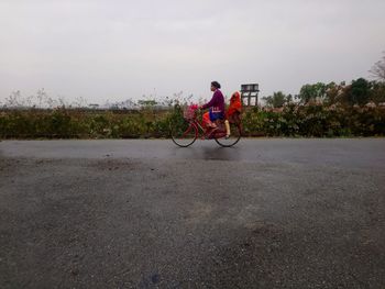 Woman with friend riding bicycle on road against sky