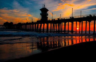 Silhouette pier over sea against orange sky