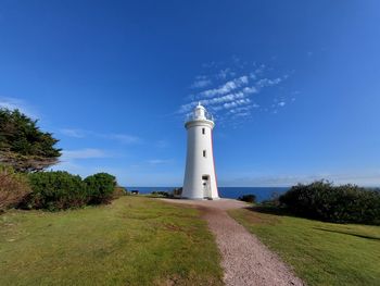 Lighthouse on field by building against blue sky