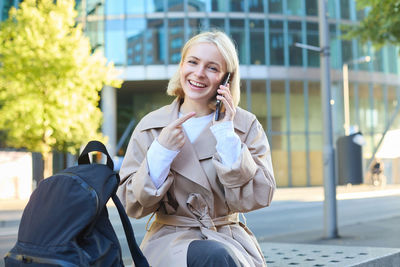 Portrait of young woman sitting on footpath in city