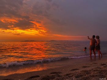 Rear view of men on beach against sky during sunset