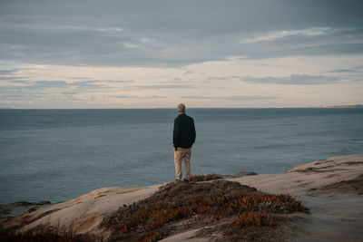 Rear view of man standing on rock by sea against sky