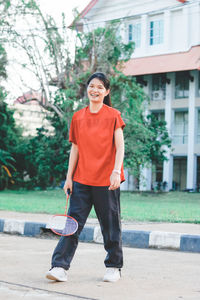 Portrait of smiling young woman holding badminton racquet while standing outdoors