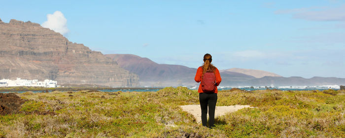 Rear view of woman walking on field against sky