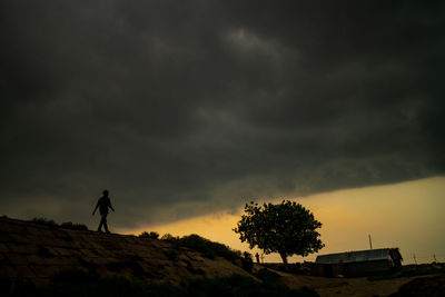 Silhouette man by tree against dramatic sky during sunset