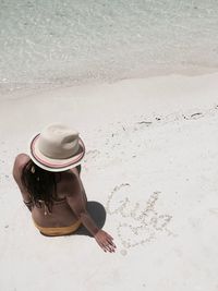 High angle view of sensuous woman wearing hat while sitting on shore at beach